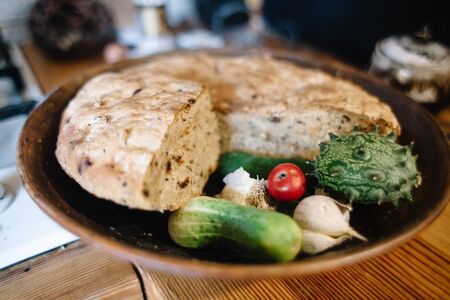 Freshly baked yeast loaf with raisins and nuts on a plate with cucumbers, tomato and garlic. Soft focus, shallow depth of field, bokeh.の写真素材