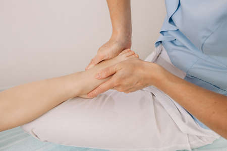 An osteopath does a foot massage to a child. Correction of the legs in the direction of a...