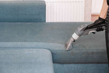 Men use a vacuum cleaner to clean the sofaの写真素材