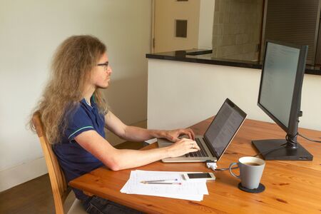 A programmer is working at home at a laptop with second monitor in his living room during Covid-19 pandemic lockdown in Londonの写真素材
