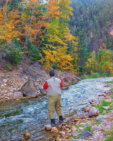Man standing on the bank of mountain river in autumn forest, fly fishingの写真素材