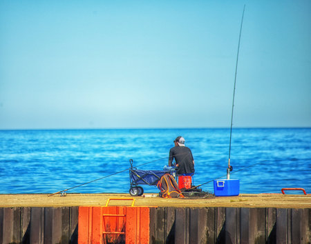 Fisherman with a fishing rod on the pier at the seaの写真素材