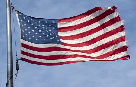 Tattered American flag flapping in the wind  on a blue sky with cloudsの写真素材