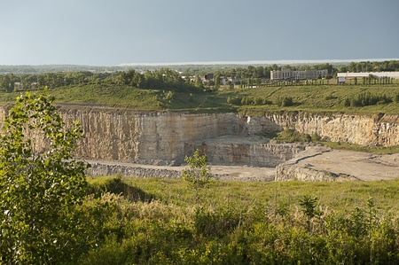 View down into a rock quarry surrounded by green hills, trees and commercial buildingsの写真素材