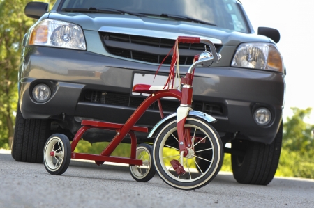 Child's tricycle dangerously parked in front of a large SUVの写真素材