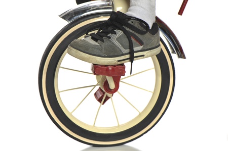 Closeup of child's foot on the pedal of red child's tricycle on a white , selective focus on the shoeの写真素材