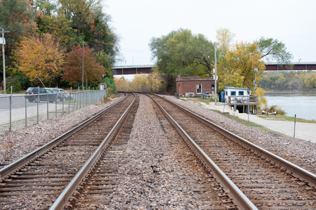Train tracks leading out of a small rural town disappear around the bend past trees covered in fall leavesの写真素材
