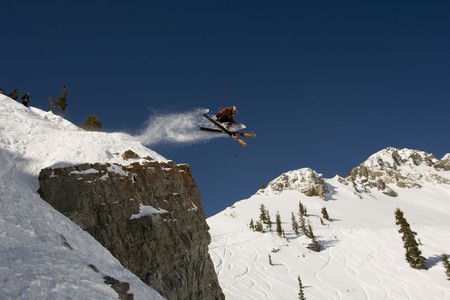 A skier jumping cross tips off cliff with mountain in backgroundの写真素材