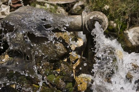 A large leaking pipe shoots water outdoors onto mossy rocks の写真素材