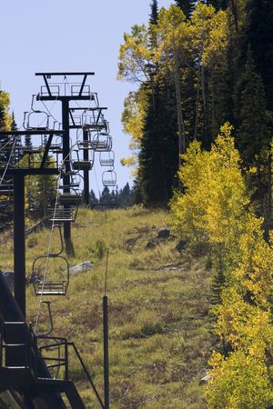 A Ski chair lift sits still next to fall colored forestの写真素材