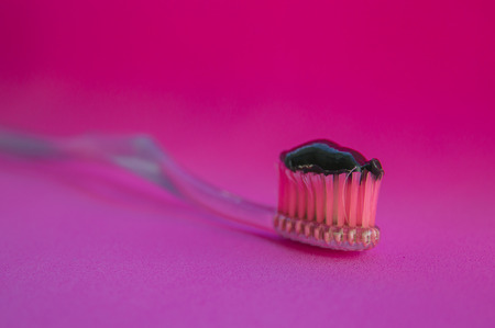 Black toothpaste on the toothbrush. Pink background.