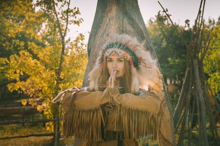 A beautiful girl in an ethnic Indian costume and in roach stands at the totem pole and holds her hands in a prayer pose.の写真素材