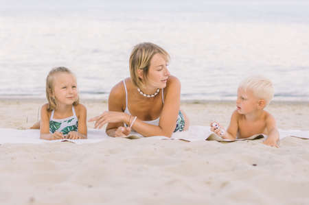 A beautiful slender mother lies with her son and daughter on a sandy beach. The river in the background.の写真素材