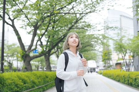 Asian young woman hydrating during exercise in urban green spaceの写真素材