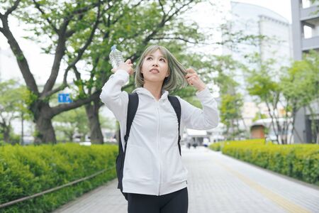Asian young woman hydrating during exercise in urban green spaceの写真素材
