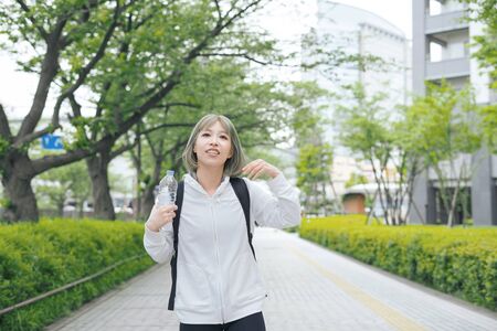 Asian young woman hydrating during exercise in urban green spaceの写真素材