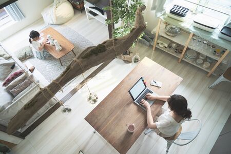 Asian mother teleworking at her table while watching her daughterの写真素材