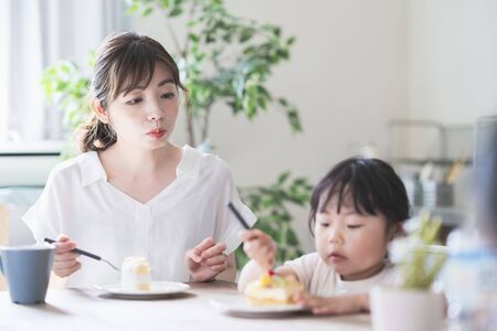 Asian mom and daughter eating cake at dining table at homeの写真素材