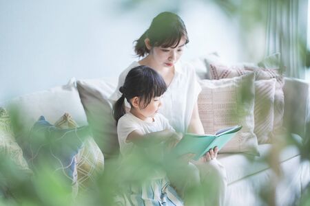 Mother and daughter sitting on the sofa and reading a picture bookの写真素材