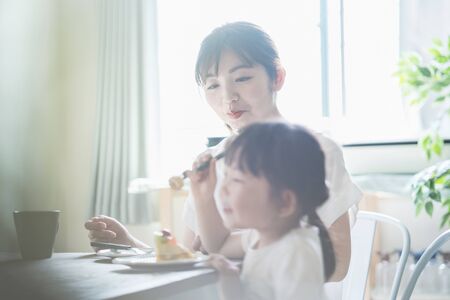 Asian mom and daughter eating cake at dining table at homeの写真素材