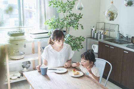 Asian mom and daughter eating cake at dining table at homeの写真素材