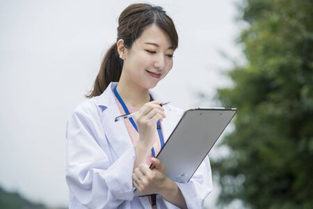 Asian female medical worker in white coat with medical chart and penの写真素材