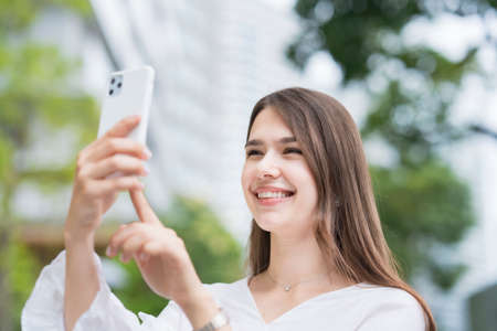 A woman touching and operating the screen of a smartphone outdoorsの写真素材