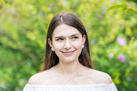 A young woman wearing a white off-shoulder shirt and surrounded by plants