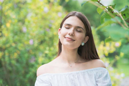 A young woman wearing a white off-shoulder shirt and surrounded by plants