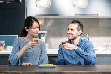 young man and woman toasting with glass of beer at homeの写真素材