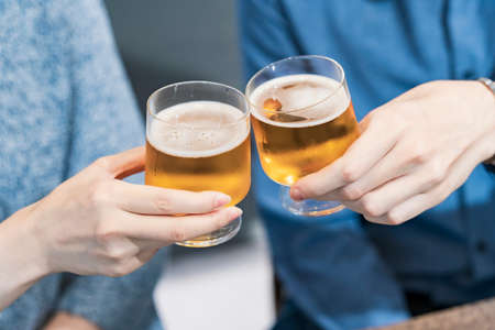 young man and woman toasting with glass of beer at homeの写真素材