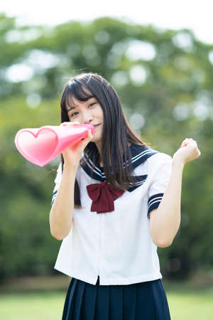 asian high school girl cheering with a heart shaped megaphoneの写真素材