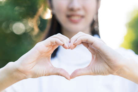 A woman in a white coat making a heart shape with both hands