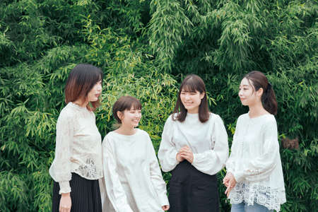 4 Japanese young women wearing white shirts and chatting in the parkの写真素材