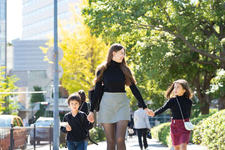Mother and two children walking outdoors holding hands with smile
