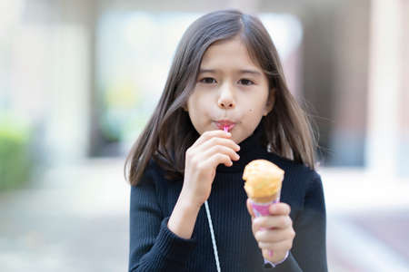 Girl eating cone type ice cream using spoon outdoorsの写真素材