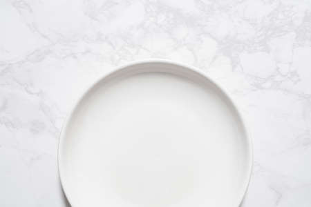 A bird's-eye view of an empty white plate placed on a marble plate