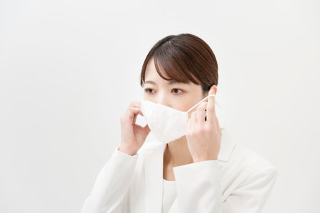 Asian woman in a white suit wearing a mask and white back groundの写真素材