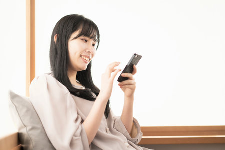 Asian woman sitting and operating a smart phone at homeの写真素材