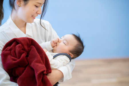 Asian young mom hugging a sleeping baby in the roomの写真素材