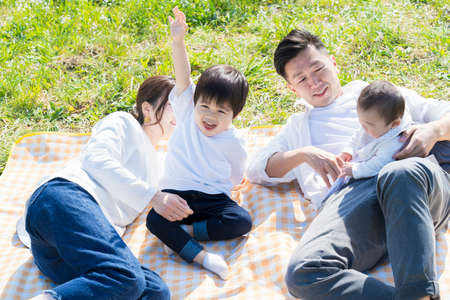 Asian parents and children enjoying a picnic on green areaの写真素材