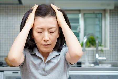 Asian middle aged woman with a tired look in the roomの写真素材