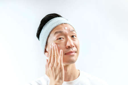 A man who applies cream to his face and white background