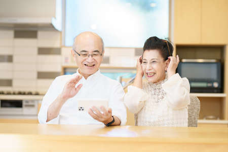 Senior couple communicating online using a smartphone in the roomの写真素材