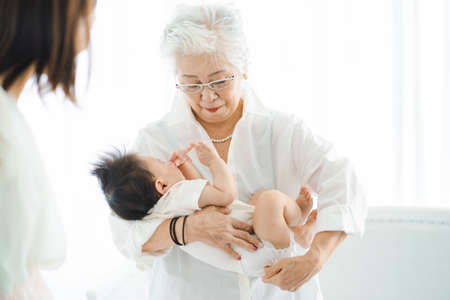 Senior woman holding a baby in a bright roomの写真素材