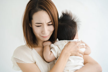 Asian mother holding a baby and looking tiredの写真素材