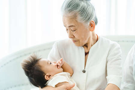 Senior woman holding a baby in a bright roomの写真素材