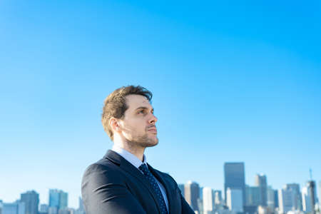 Portrait of a businessman, blue sky and buildings of big cityの写真素材