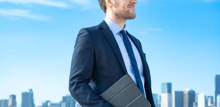 A businessman against the backdrop of the blue sky and buildingsの写真素材