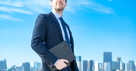 A businessman against the backdrop of the blue sky and buildingsの写真素材
